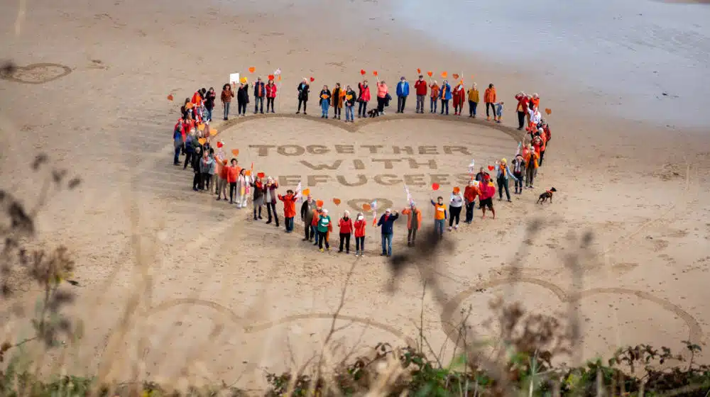 people forming heart on beach for refugee support
