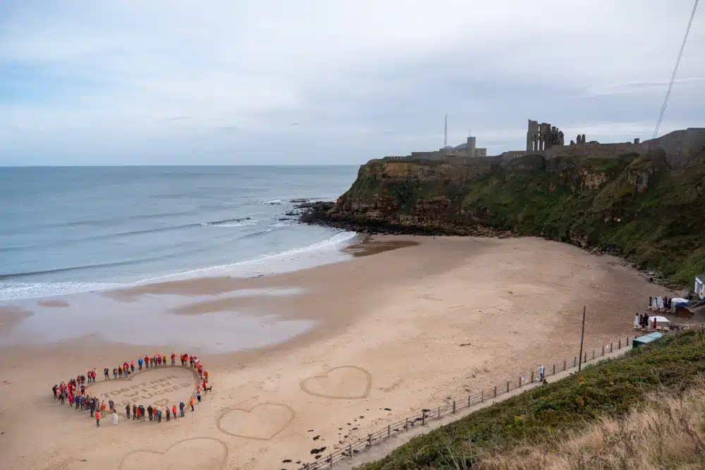 people forming heart on beach for refugee support 2